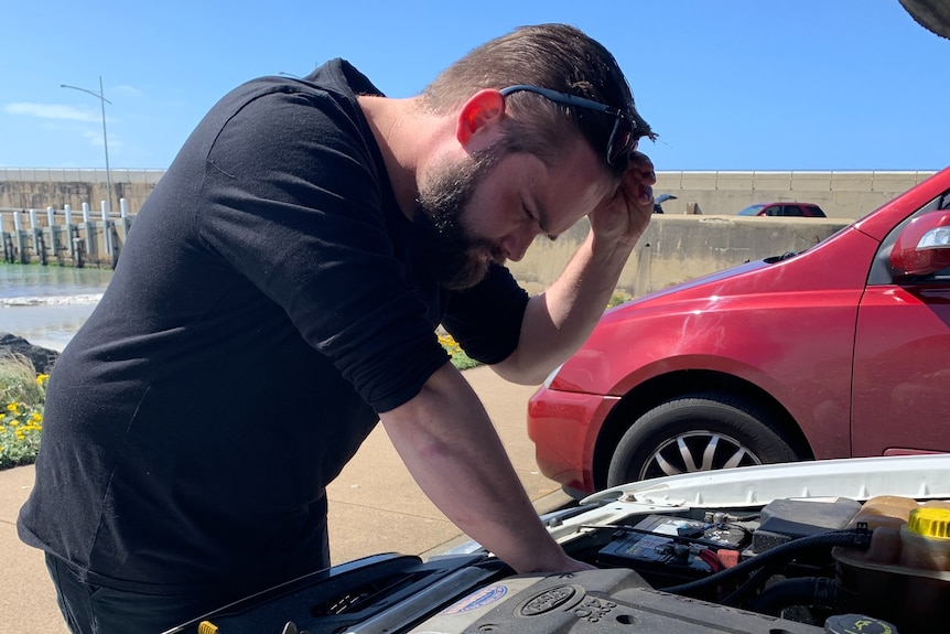 Damon Ridge looks into the bonnet of his car with his glasses on his head.