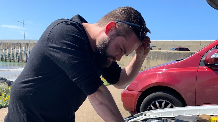 Damon Ridge looks into the bonnet of his car with his glasses on his head.