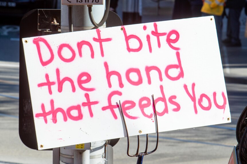 A protest sign says 'don't bite the hand that feeds you'.