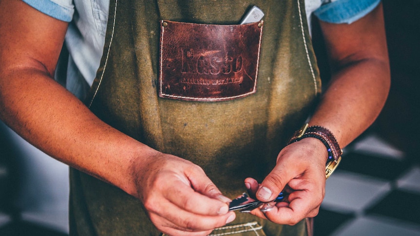 A worker in a leather apron hold a set of tools in his hands.