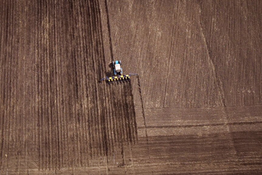 A drone shot of a tractor in a dirt field 