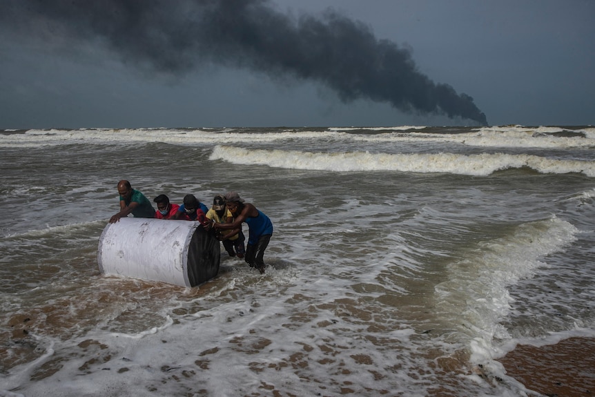 Locals salvage a container washed to shore from the burning ship 