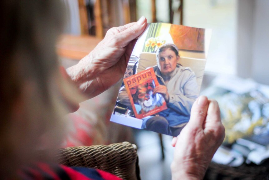 An older woman's hands hold a photo of her 51-year-old daughter, who is severely disabled.