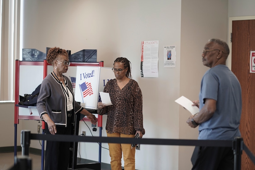 Three people stand in a hall voting.