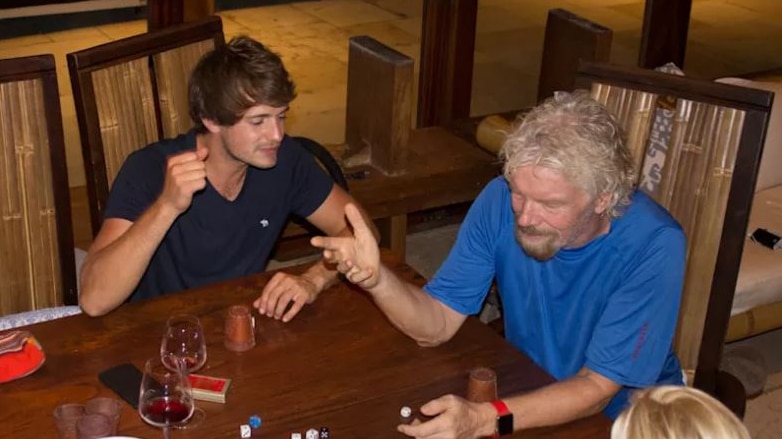 Richard Branson sits at a table covered in wine and dice with members of his staff.