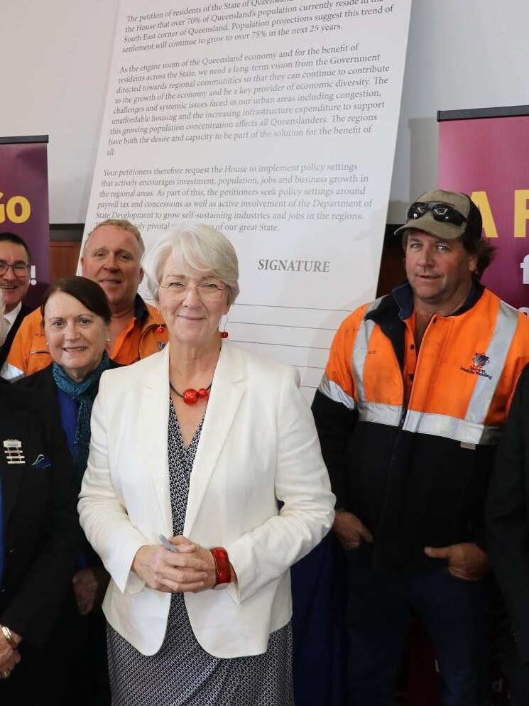 A group of local government representatives stand in front of a poster and banners stating "Fair Go for All Queenslanders".