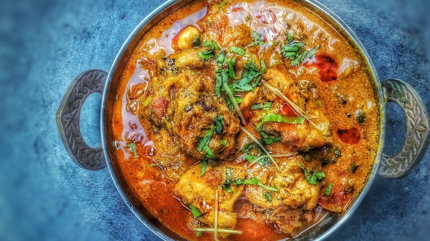 bowl of chicken curry in a metal dish, photographed from above.