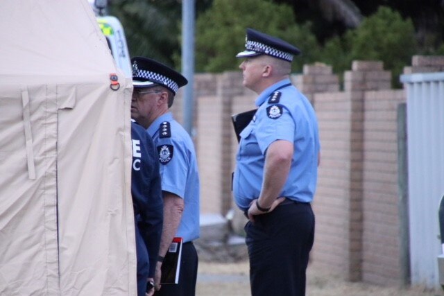 Two police officers in uniform stand next to a canopy on a suburban street.