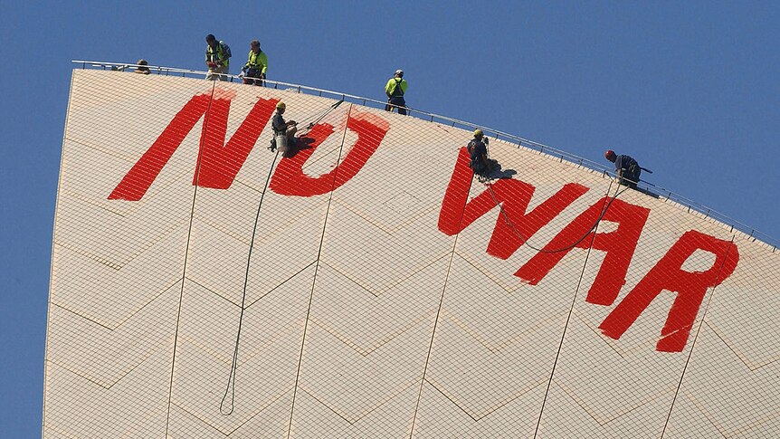 Two men abseil off the top of the Sydney Opera House and paint over large red letters spelling 'NO WAR'