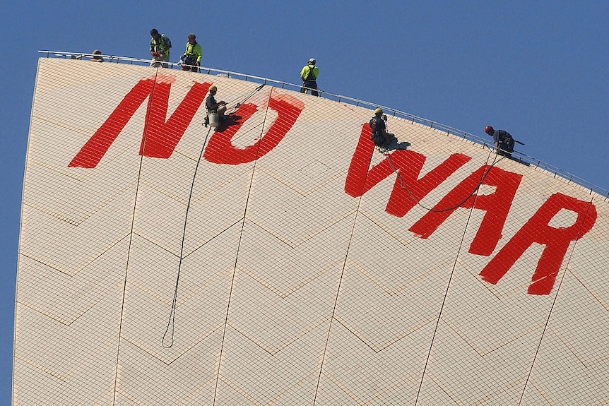 Two men abseil off the top of the Sydney Opera House and paint over large red letters spelling 'NO WAR'