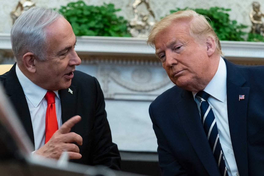 Benjamin Netanyahu looks at Donald Trump mid-speech and waves a finger as he sits next to Donald Trump as he looks down.