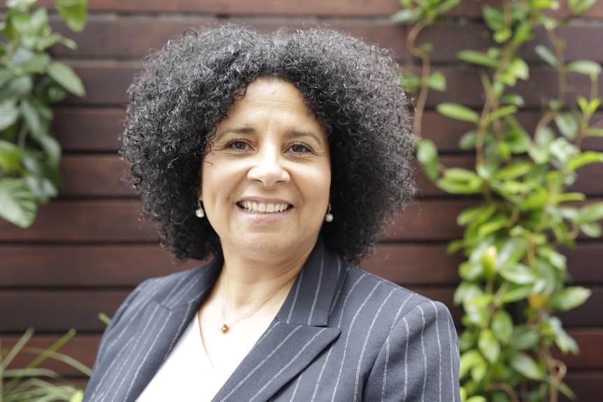 A smiling, formally dressed woman with dark, curly hair.