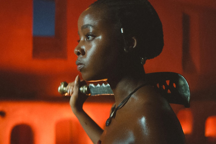 A side profile of a black woman holding a machete on her shoulder.