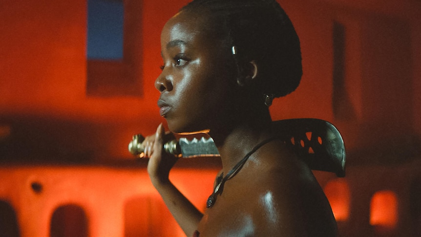 A side profile of a black woman holding a machete on her shoulder.