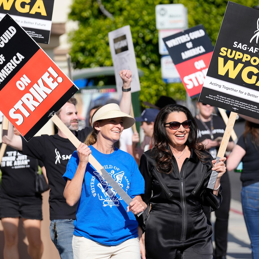 Fran Drescher in black velvet tracksuit and Meredith Stiehm in blue T smile while holding protest signs