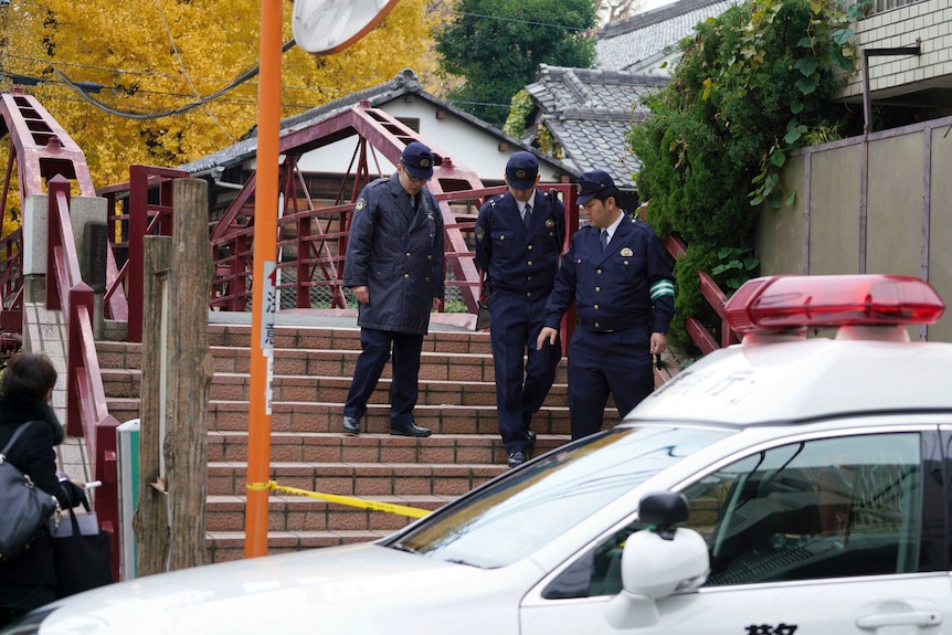 Three police officers standing on steps in front of a shrine.