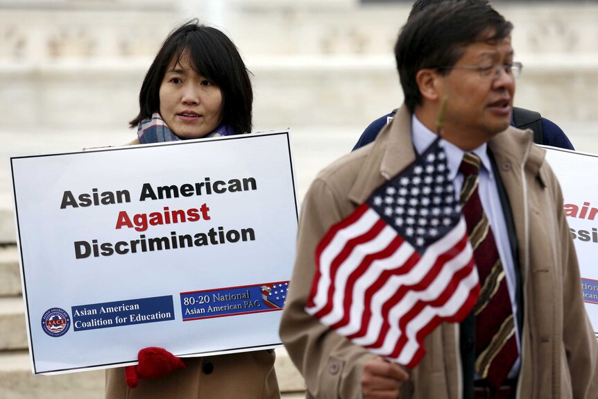 A woman holds a placard saying 'Asian American against discrimination'.
