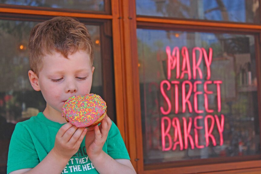 A young boy enjoys a rainbow donut.