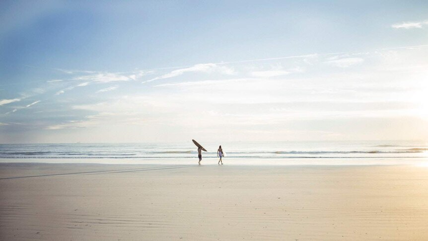 Two people carrying surfboards walk towards a calm ocean.
