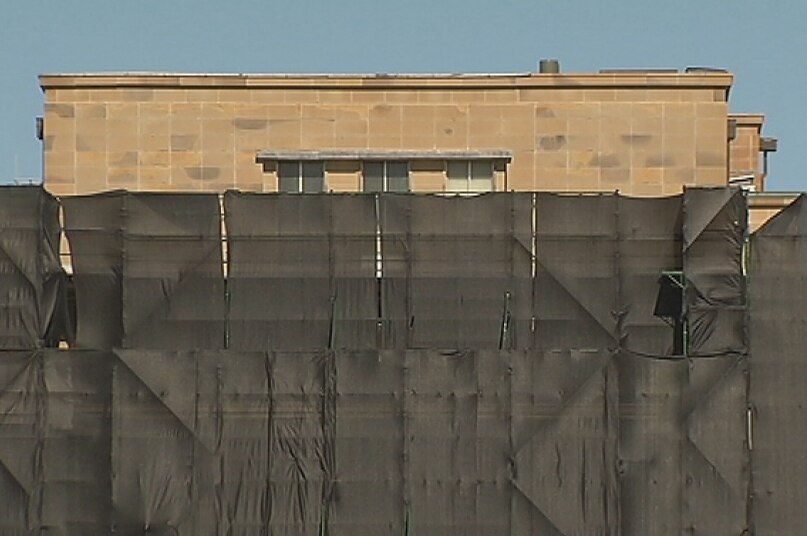 The top section of the John Gorton building is just visible above the safety hoarding.