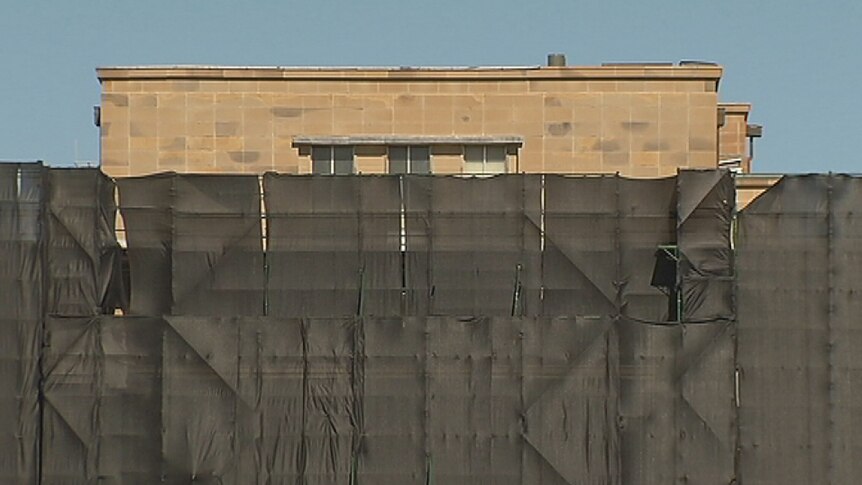 The top section of the John Gorton building is just visible above the safety hoarding.