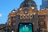 A phone screen showing the time 6.25 is in front of the analog flinders st station clock showing 6.20