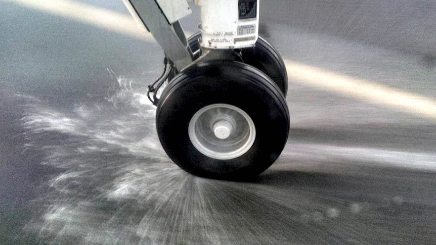 Plane wheel sprays water as it hits the runway.
