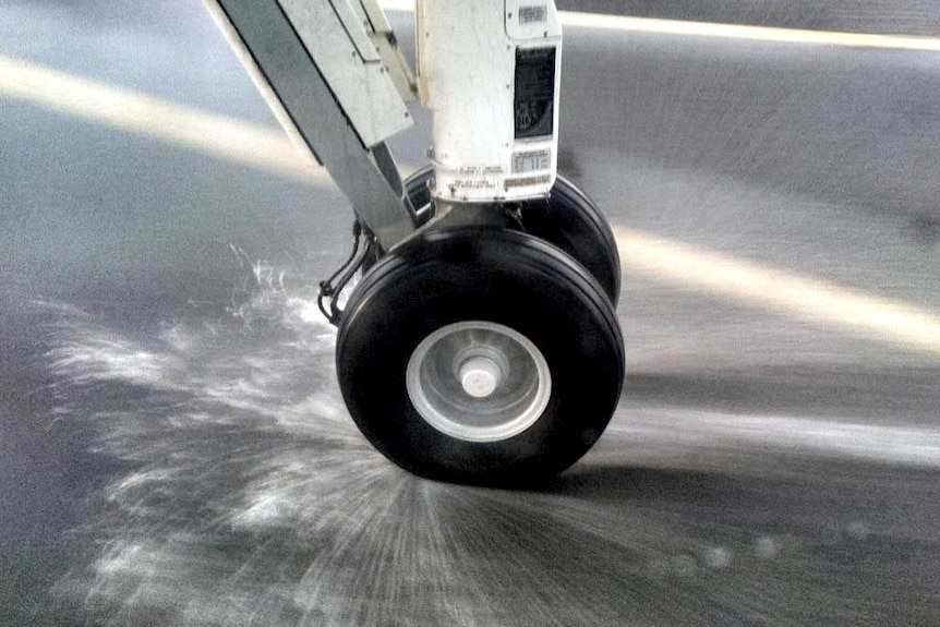 Plane wheel sprays water as it hits the runway.