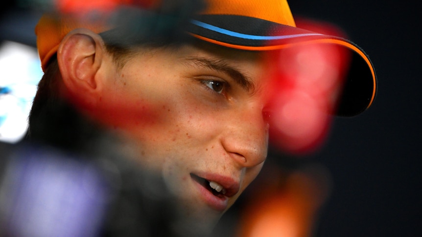 A young man in an orange cap, at night, talking to media, with reflective light obscuring his face.