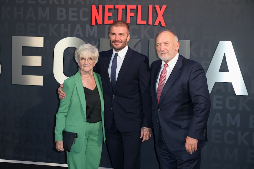 David Beckham stands with his arms around Ted and Sandra at a Netflix event