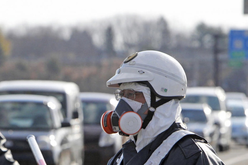 A Japanese official wearing a helmet and facemask directs traffic.
