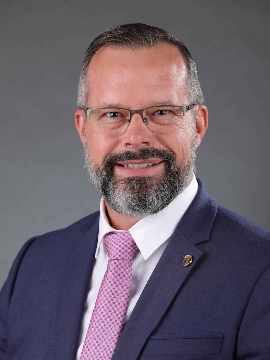 a graying man in glasses and a suit smiles at the camera