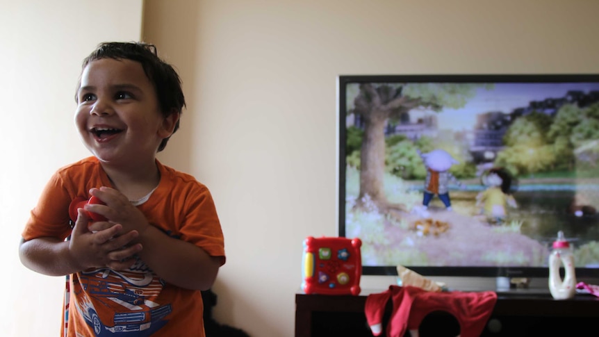 Two-year-old Nayte Slater laughs and clutches a toy at the Gomeroi gaaynggal centre in Tamworth.