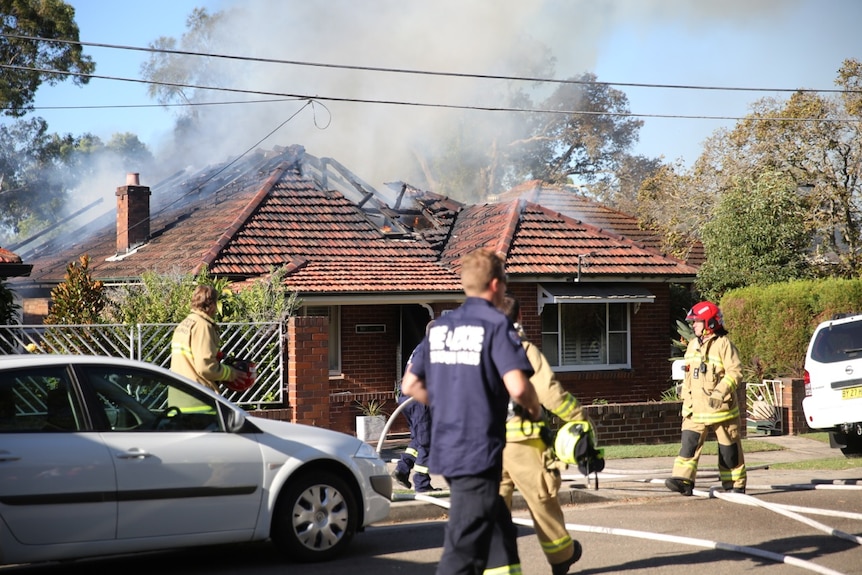 Firefighters outside a one-story brick home on fire.