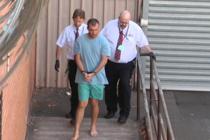A man in handcuffs is walking flanked by two security guards
