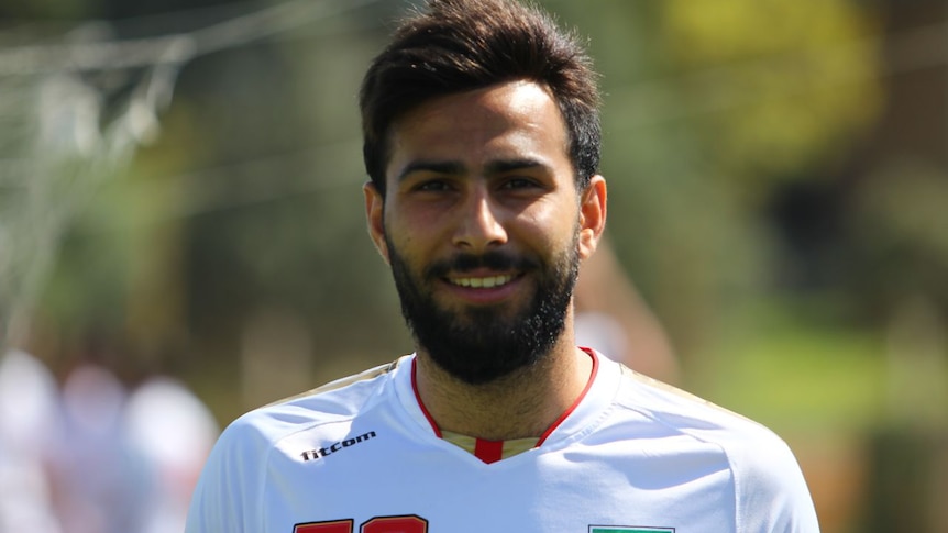 Amir Reza Nasr Azadani smiles at the camera while wearing a football uniform.