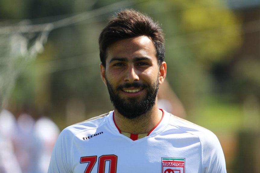Amir Reza Nasr Azadani smiles at the camera while wearing a football uniform.