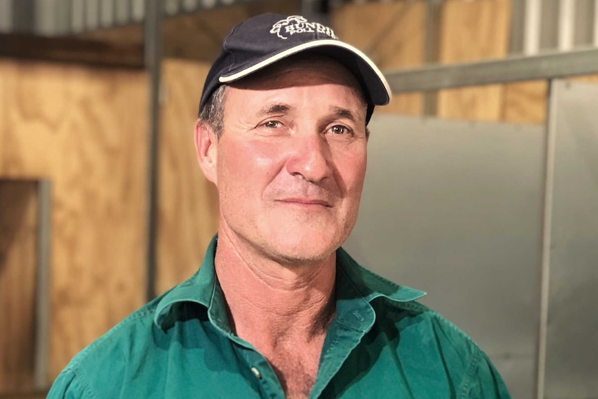 Farmer David Young on his farm smiling, wearing a baseball cap and green shirt.