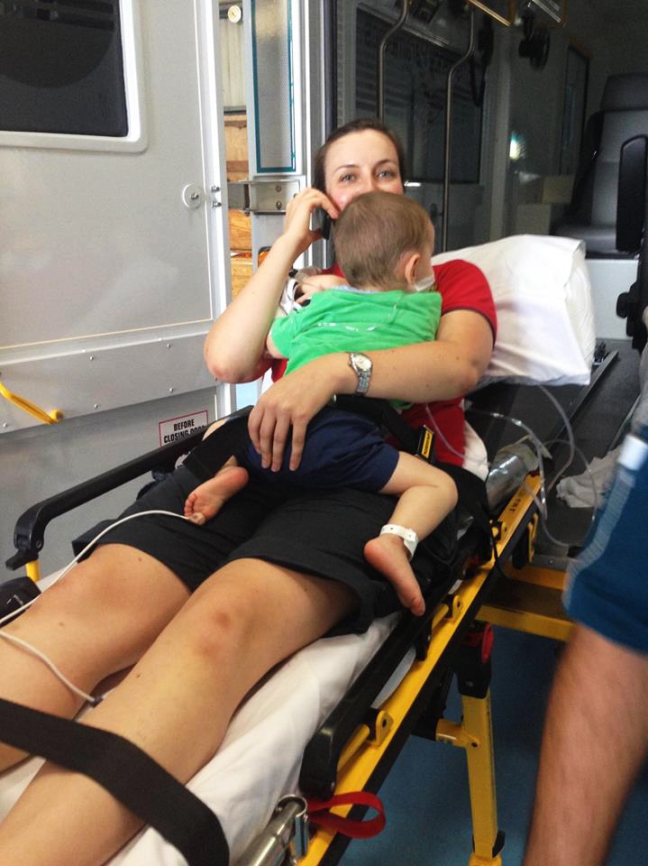 A midwife on an ambulance stretcher cradles a toddler while on the phone