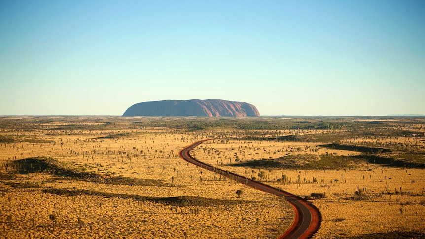 Uluru in the distance with a road winding its way towards it.