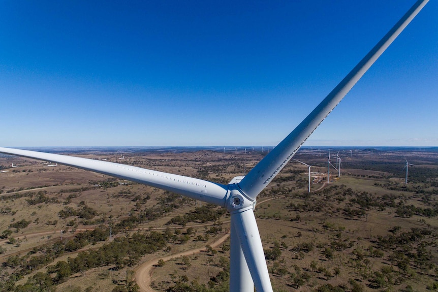 A drone shot of a large wind turbine with dozens of other turbines in the background.