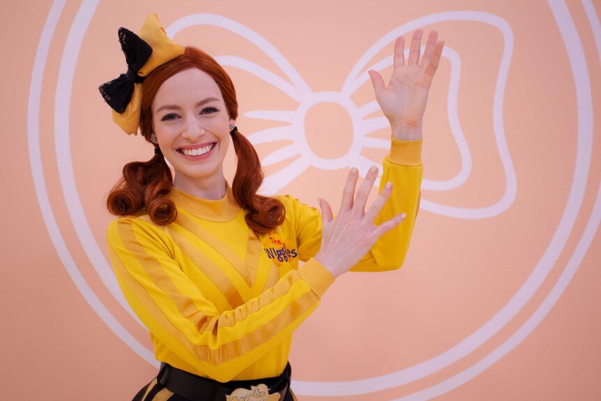 Female red haired children's entertainer wearing bright yellow top conducting sign language.