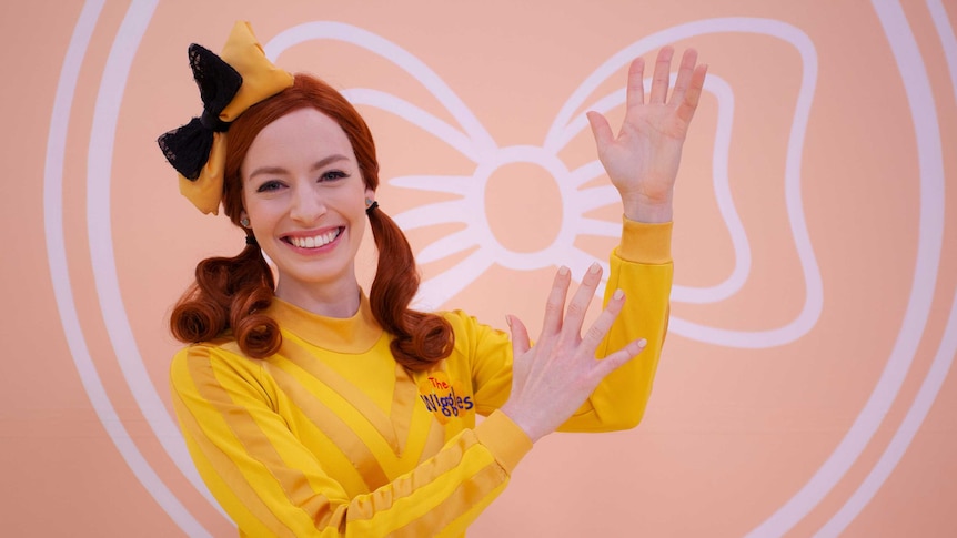 Female red haired children's entertainer wearing bright yellow top conducting sign language.