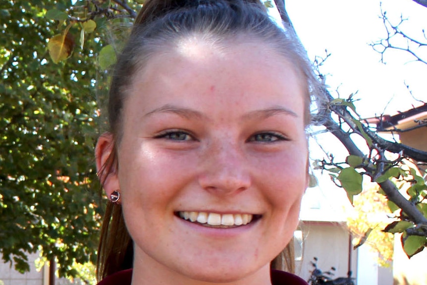 Seventeen year old, Tori Voumard, smiling in school uniform in front of tree.