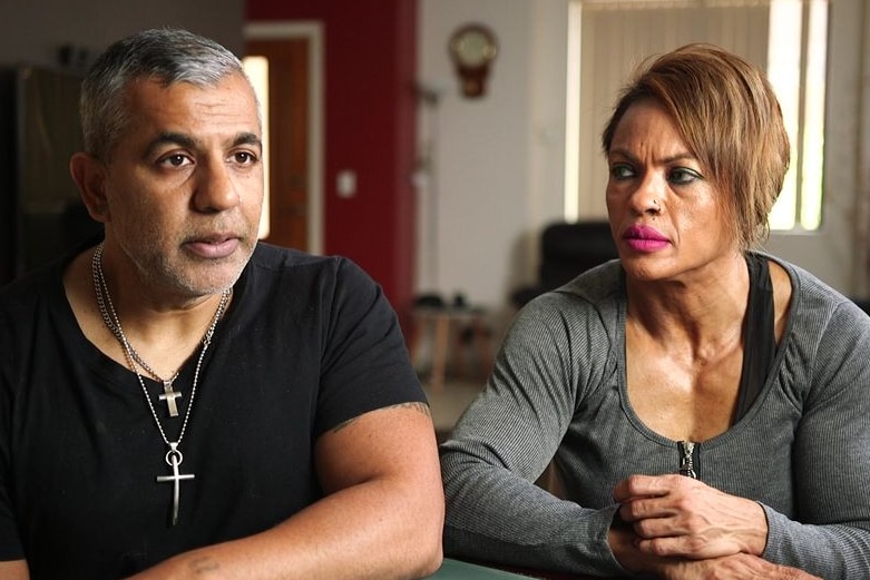 A man and a woman sitting at a table. The man is wearing two crucifix necklaces.