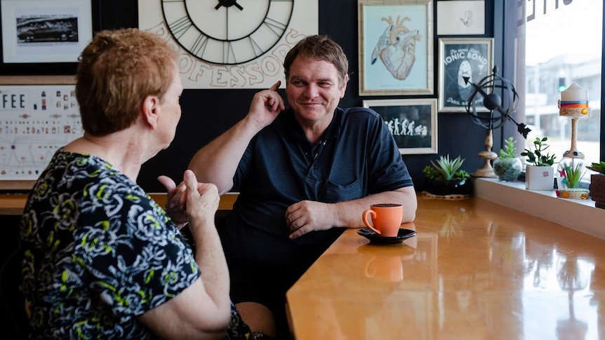 A man uses sign language to an older lady while they have a coffee.