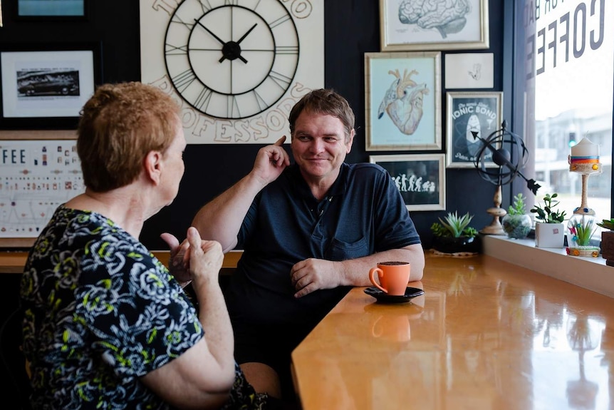 A man uses sign language to an older lady while they have a coffee.