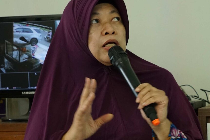 Dewi Hestyawati sits on the floor and speaks into a microphone.