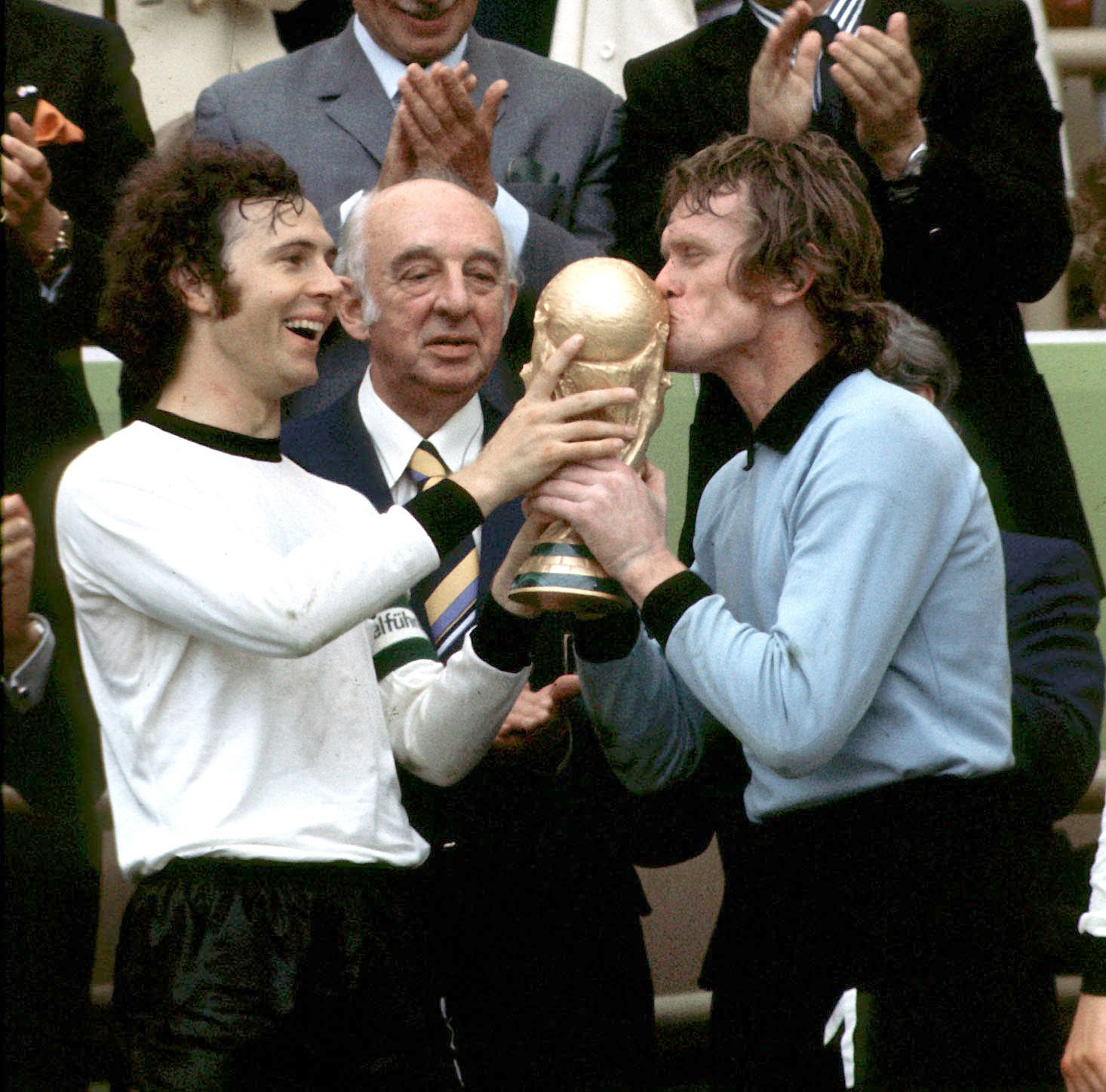 Two soccer players hold and kiss a trophy