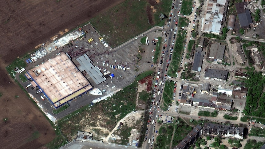 A satellite image shows people waiting in queues outside a large  building